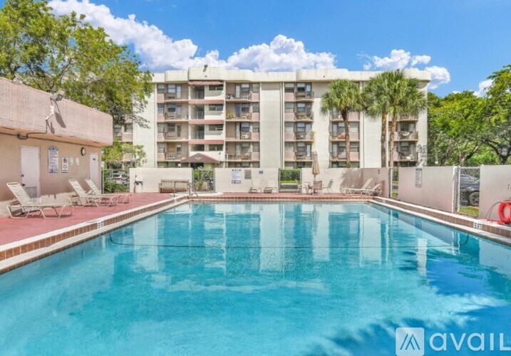 A large swimming pool in front of a multi-story apartment building with a clear blue sky above.
