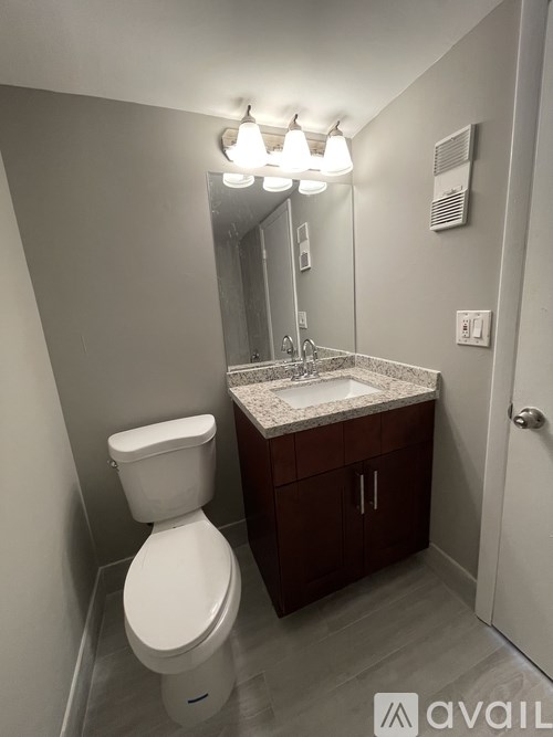 A white toilet is in a bathroom with a marble counter top and a mirror above it.