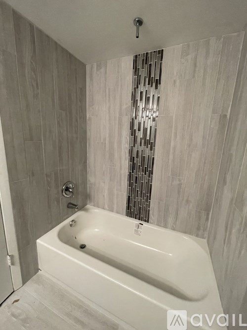 A white bathtub in a bathroom with a grey tiled wall.