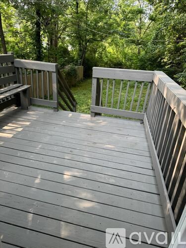 A wooden deck with a bench and railing overlooking a wooded area.