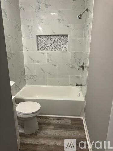 A white toilet sits next to a bathtub in a bathroom with marble tile walls.