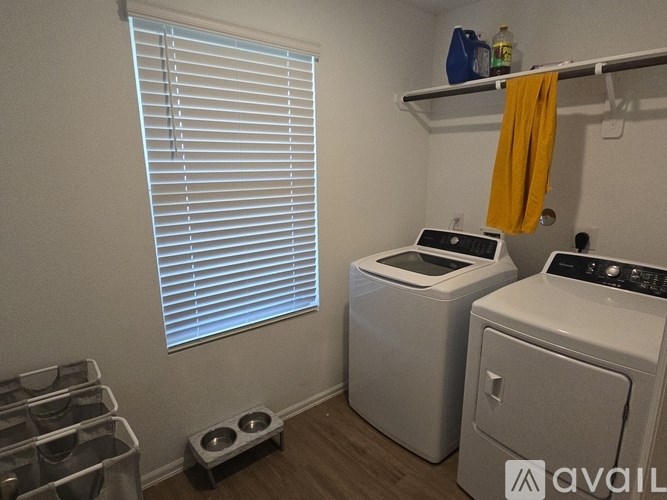 A laundry room with a washer and dryer, a window with blinds, and a shelf with a yellow towel hanging on it.