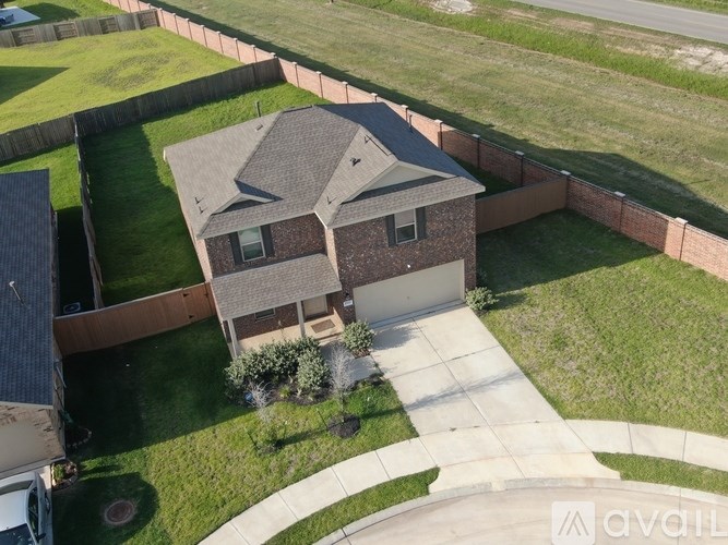 A house with a brown roof and a white garage door is surrounded by a brick wall and a green lawn.