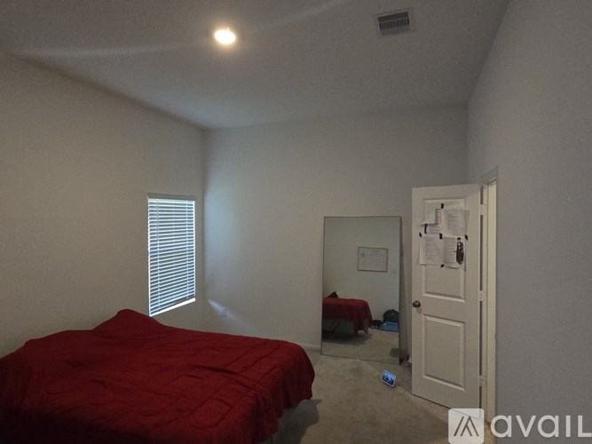 A bedroom with a red bedspread and a white door.