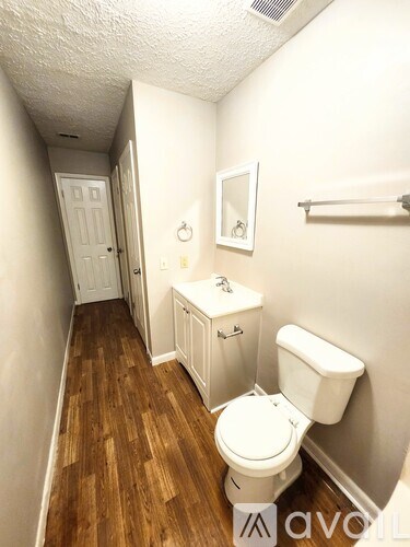 A white toilet in a small room with wood flooring.