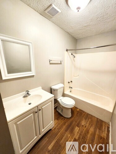 A white bathroom with wood flooring and a white toilet.