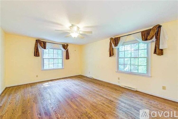 A room with wooden floors and two windows with curtains.