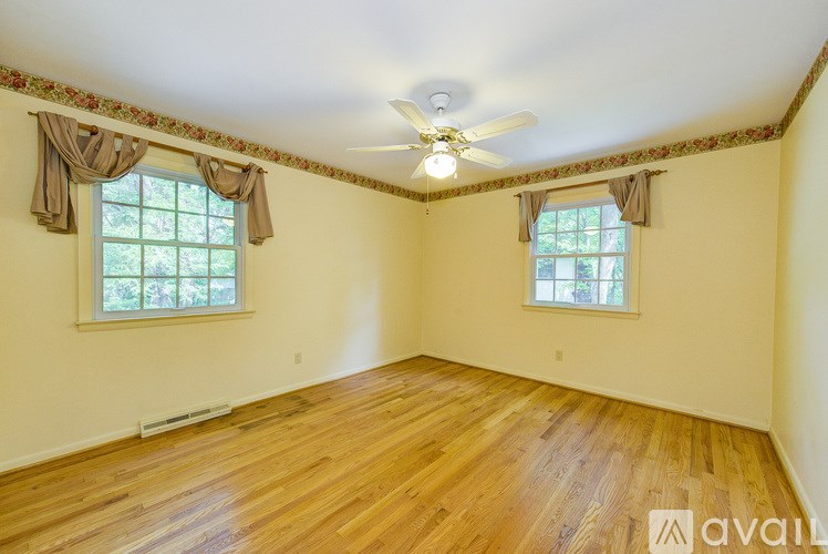 A room with wooden floors and two windows with curtains.