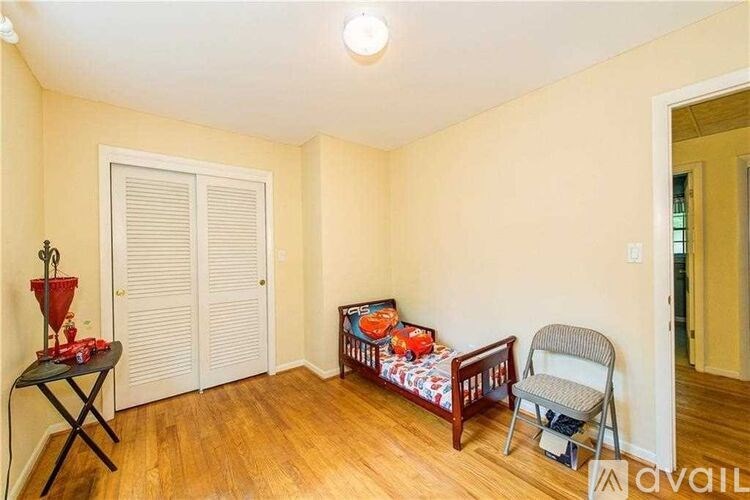 A room with a bed, a chair, and a table with a vase on it.