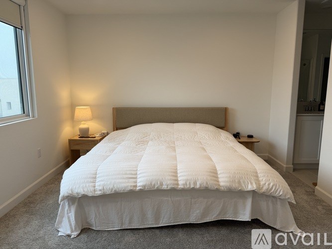 A bed with a white comforter is in a room with a carpeted floor.