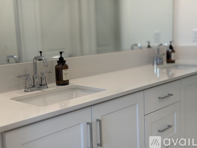 A bathroom with a white countertop and a sink with a soap dispenser on it.