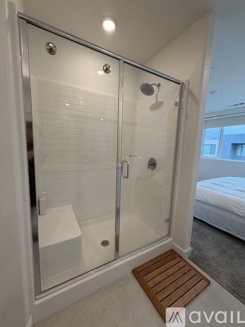A glass shower stall with a wooden mat in front.