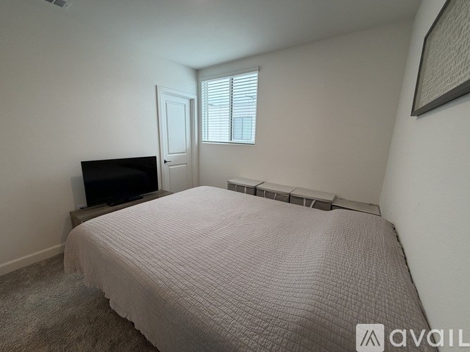 A bedroom with a bed, a television, and a window with blinds.