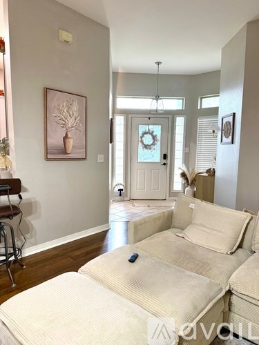 A living room with a white couch and a painting of a plant on the wall.