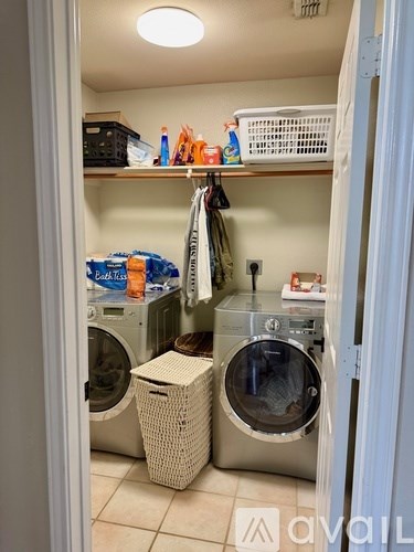 A laundry room with a washer and dryer, a basket, and a shelf with various items.