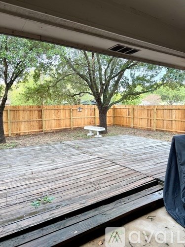 A wooden deck with a bench and trees in the background.
