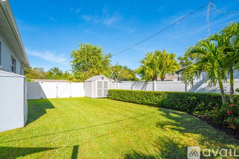 A sunny day in a well-kept backyard with a white fence and a small building.