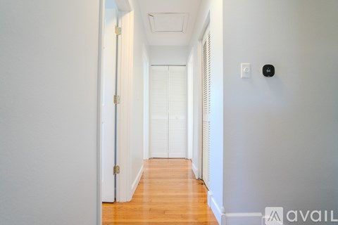 A long hallway with a door on the left and a wall-mounted device on the right.