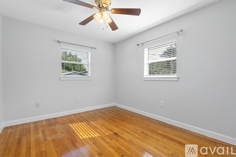 A room with a ceiling fan and two windows.