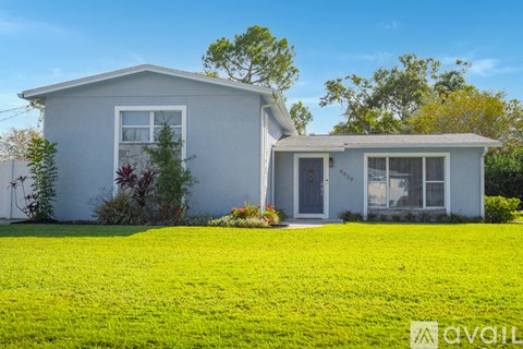 A house with a white exterior and a grey roof is surrounded by a green lawn.