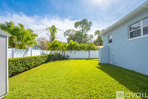A sunny day in a backyard with a white fence and green grass.
