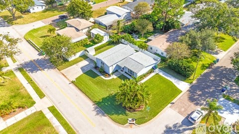 A large white house with a grey roof is surrounded by a well-maintained lawn and trees.