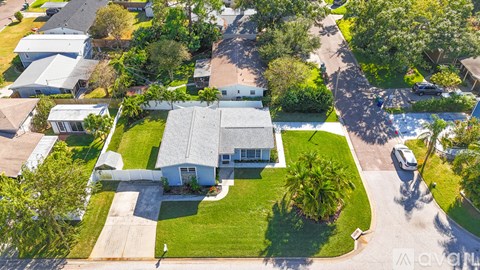 A house with a grey roof is surrounded by a green lawn and trees.