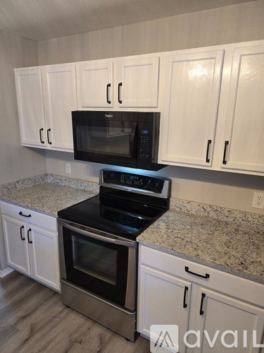 A kitchen with white cabinets and a black microwave above a stove.