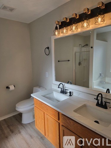 A bathroom with a toilet, sink, mirror, and lights.