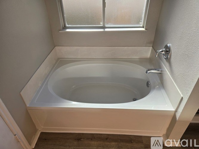 A white bathtub is installed in a bathroom with a window above it.