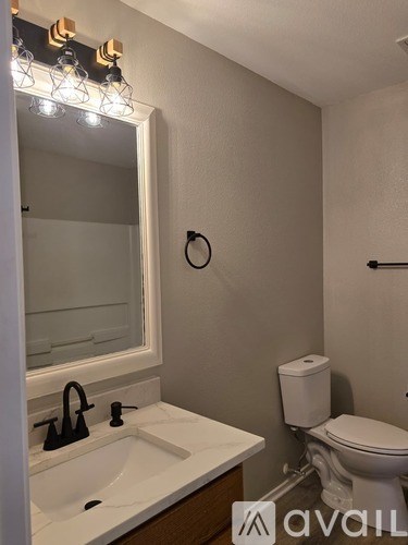 A bathroom with a toilet, sink, mirror, and lights.