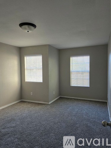 A room with carpeted floor and two windows with blinds.