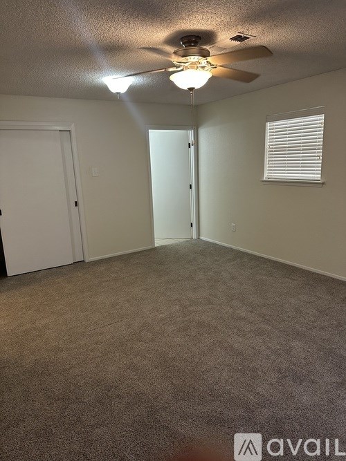 A room with a carpeted floor, a ceiling fan, and a door.