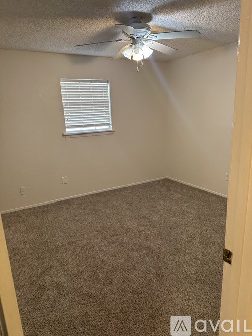A room with a carpeted floor, a ceiling fan, and a window with blinds.