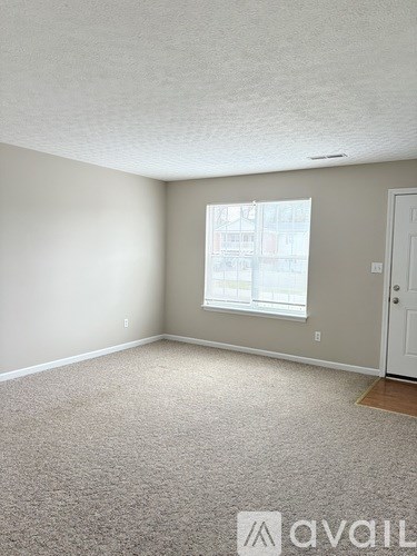 A room with a carpeted floor and a window with a view of buildings outside.