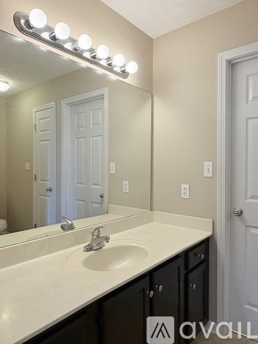 A bathroom with a vanity and a mirror with lights above it.
