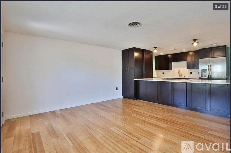 A spacious room with wooden flooring and a kitchen area in the background.