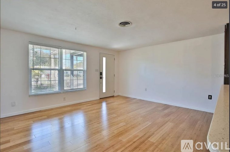 A spacious room with wooden flooring and a window with blinds.
