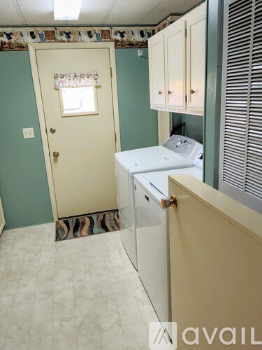 A white washing machine sits in a laundry room with a green wall and a door with a window.