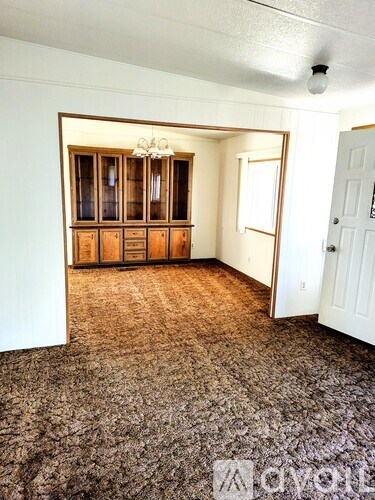 A room with a carpeted floor and a wooden cabinet with glass doors.