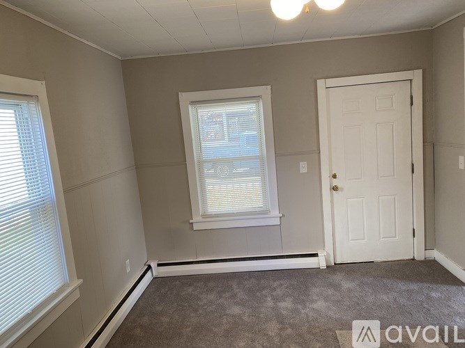 A room with a carpeted floor, a door, and a window with blinds.