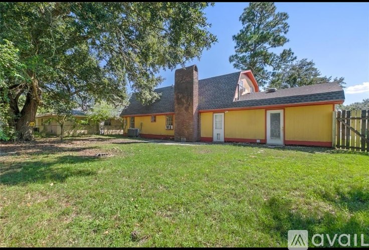 A yellow house with a red roof is surrounded by green grass and trees.