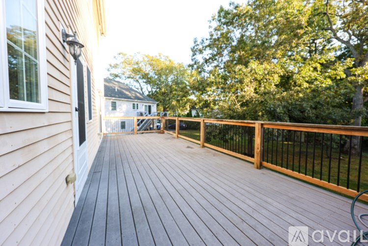 A wooden deck with a black railing and a tree in the background.