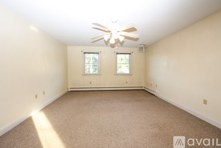 A spacious room with a ceiling fan and two windows.