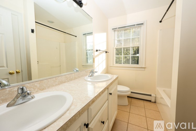 A bathroom with a sink, mirror, toilet and window.
