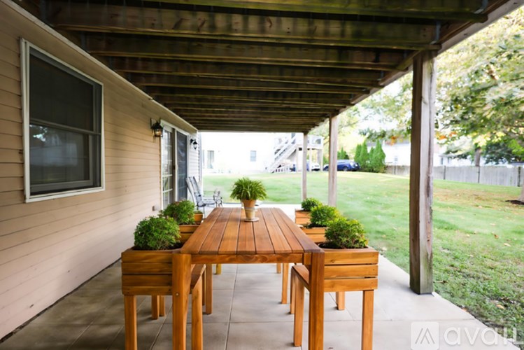 A wooden table with four chairs and a potted plant on each chair is on a patio.