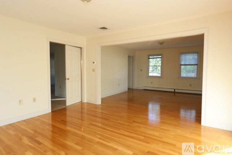 A room with wooden floors and white walls, with a door on the left and a window on the right.