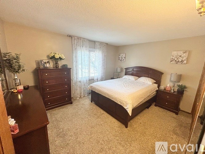A bedroom with a large bed, a dresser, and a nightstand with a lamp.
