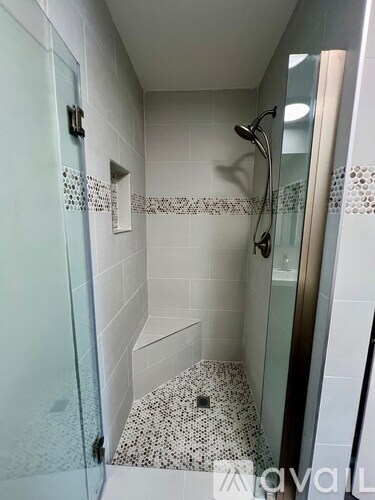 A white tiled shower with a glass door and a shower head.