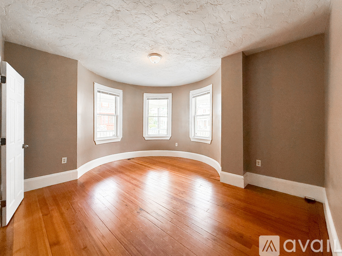A room with wooden floors and three windows.